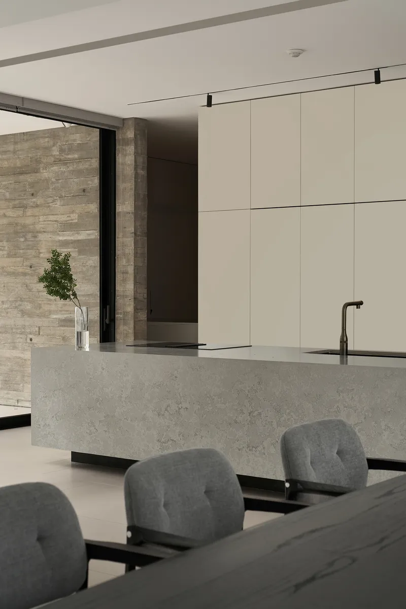 Terrazzo island with black sink and faucet facing travertine wall beyond glass door