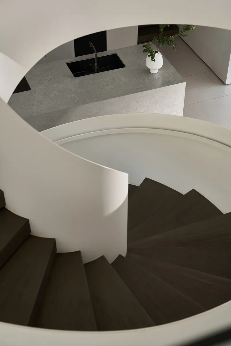 Top-down view of spiral staircase with dark treads and terrazzo island visible above