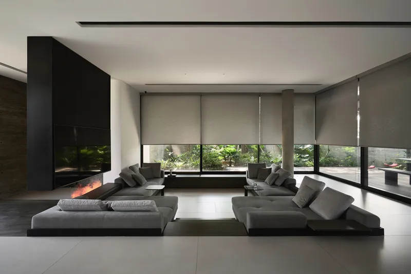 Living room with low grey seating and roller shades filtering daylight from garden beyond