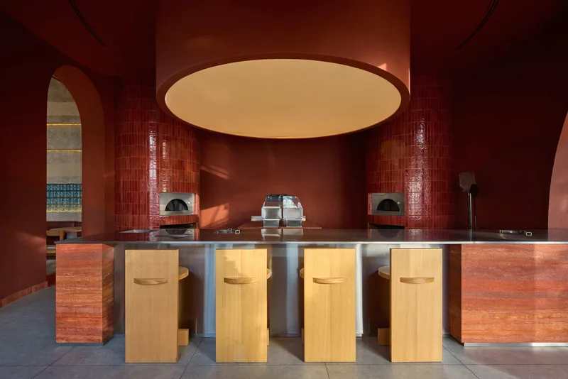 Counter with timber stools and stainless steel base beneath a circular ceiling recess in red-tiled interior