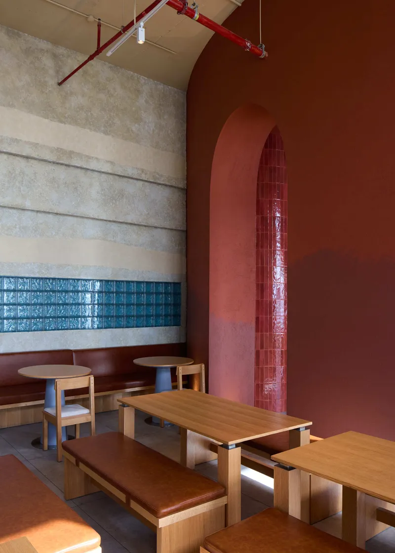 Corner detail of arched alcove with red glazed tile niche beside timber benches and exposed red conduit