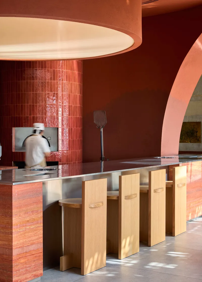Counter with timber stools beneath a circular pendant light in a terracotta-toned interior with sunlight streaming in