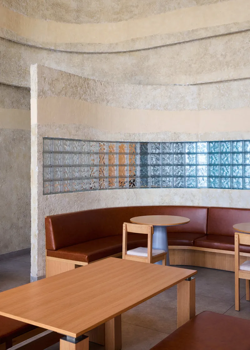 Built-in banquette seating with timber tables beneath a horizontal band of glass block windows