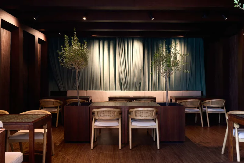 Dining area with dark timber paneling and cane-backed chairs beneath exposed ceiling beams and illuminated fabric drapes