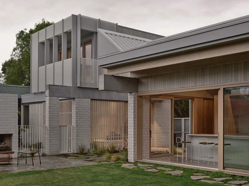 Rear courtyard showing the two-story corrugated metal volume above stacked brick walls at dusk