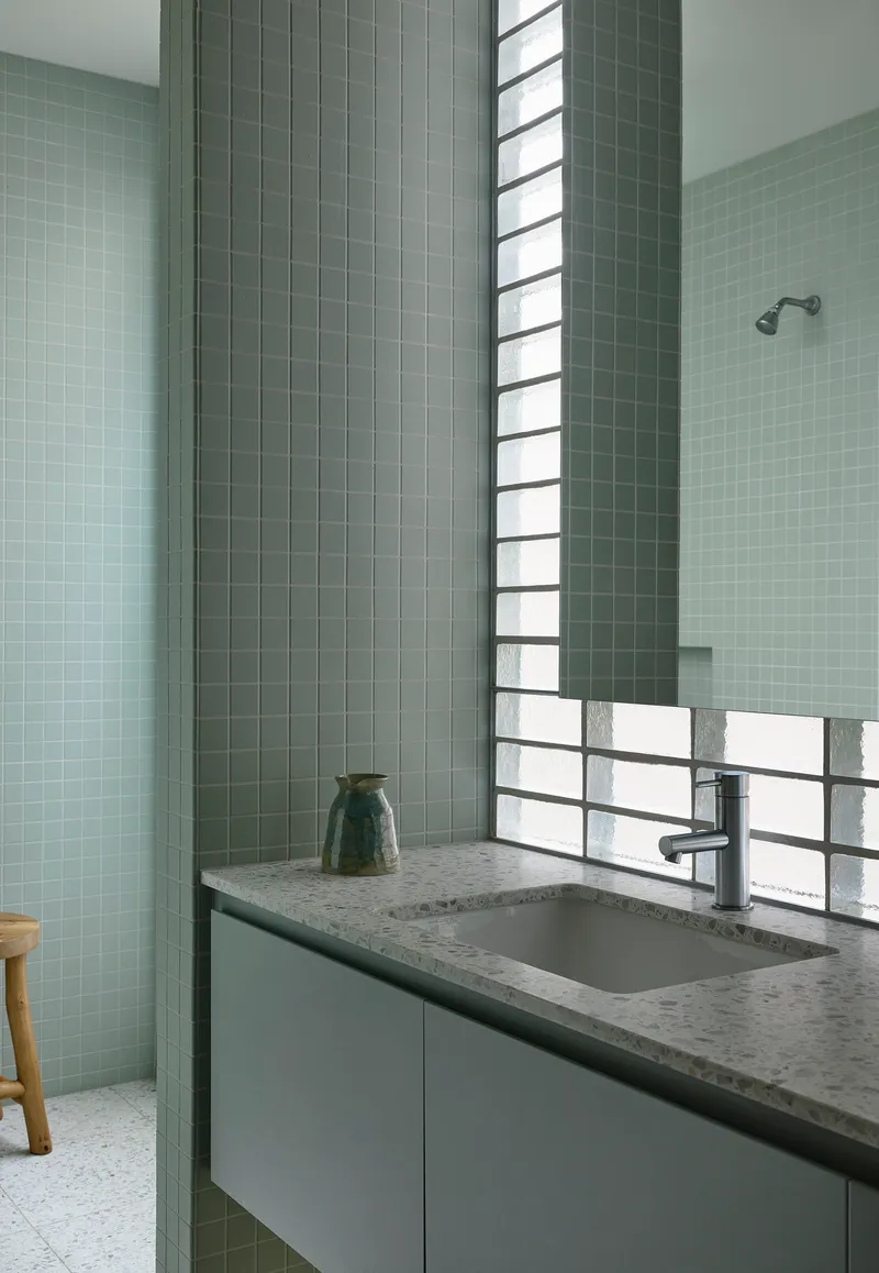 Vanity with terrazzo countertop beneath a horizontal glass block window flanked by sage green tile walls