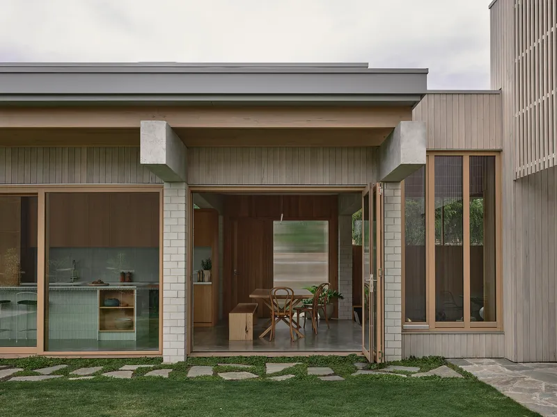 Rear facade with concrete beams sheltering glazed openings and stone paver path through lawn