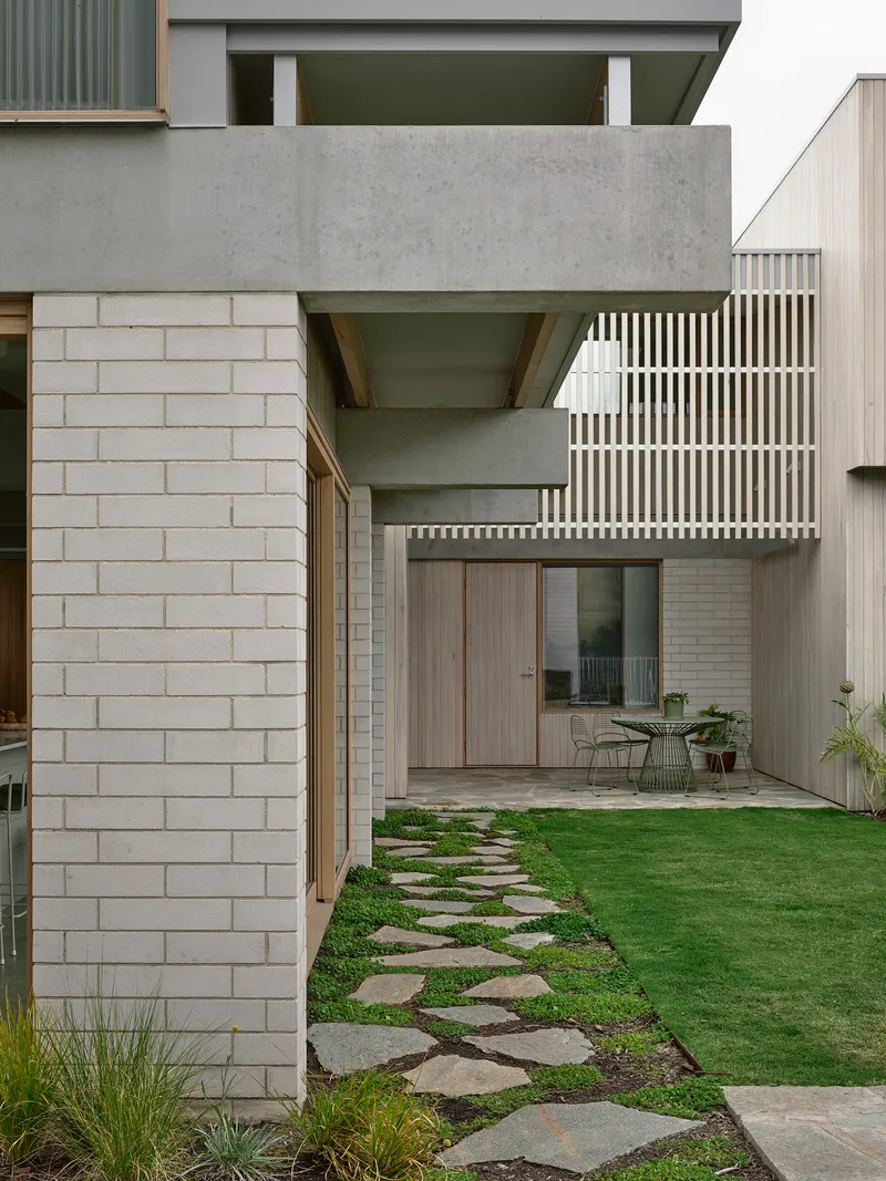 Concrete canopy projecting over lawn with stepping stone path leading to courtyard beyond
