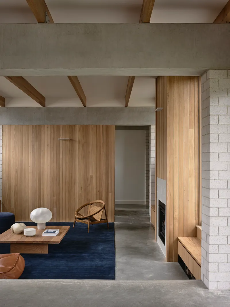 Living room with exposed timber beams, vertical wood paneling, white brick fireplace, and blue rug