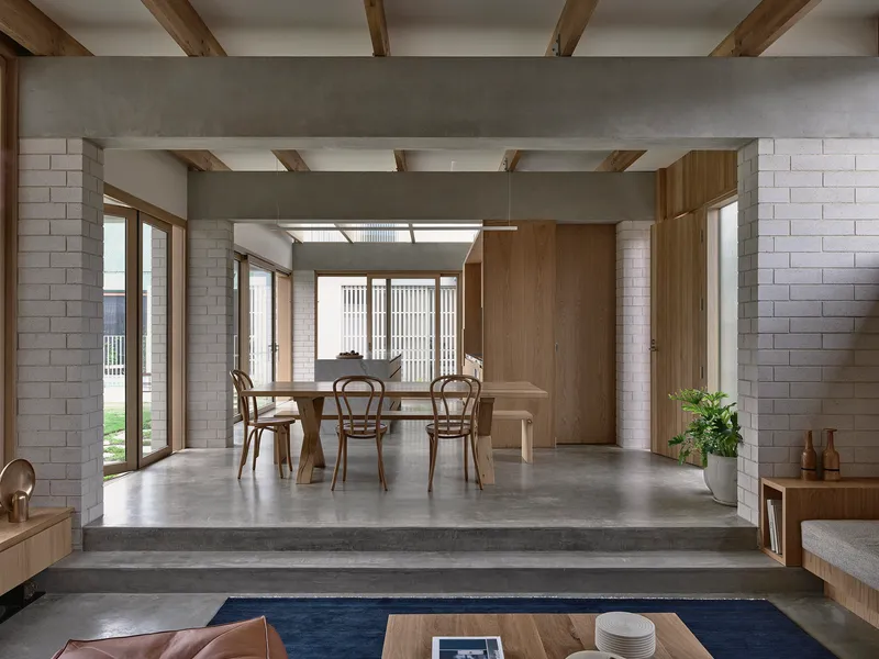 Dining area with timber table and chairs beneath exposed ceiling beams and vertical timber screen beyond