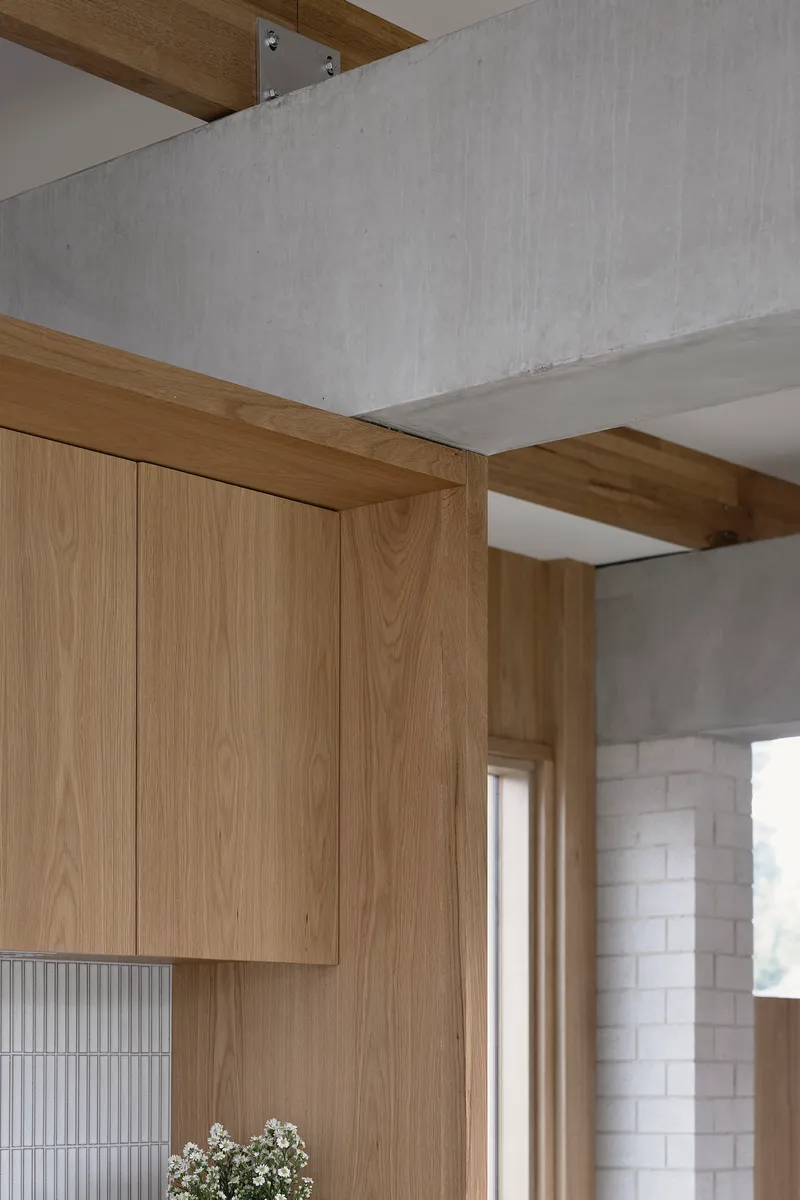 Detail of timber cabinetry meeting concrete beam with ribbed tile backsplash and white brick wall visible