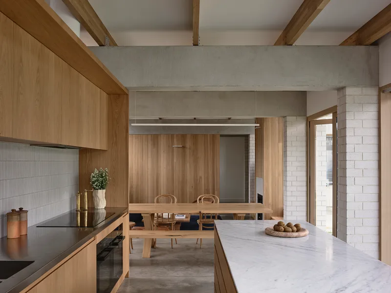 Kitchen with timber cabinetry, marble island, and view through to dining area with concrete beams overhead
