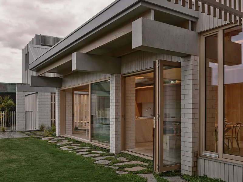 Close-up of cantilevered concrete beam over glazed doors with stepping stones through lawn
