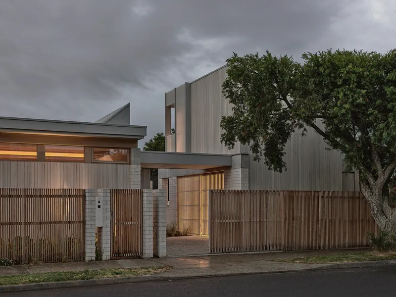 Entry courtyard with timber slatted gate and vertical screen fence beside an old tree at twilight