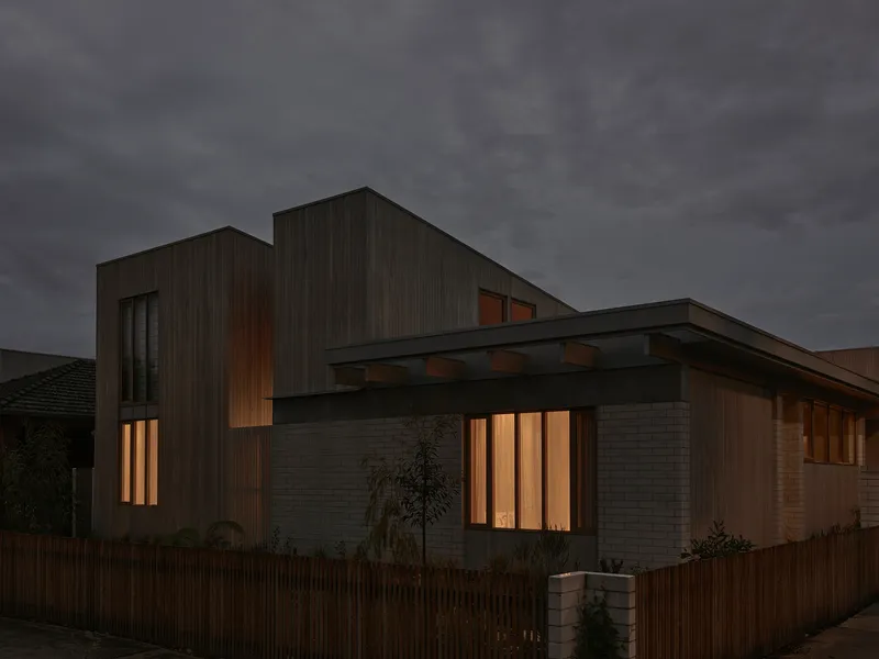 Street view of the timber-clad facade with vertical slatted windows glowing warmly at dusk