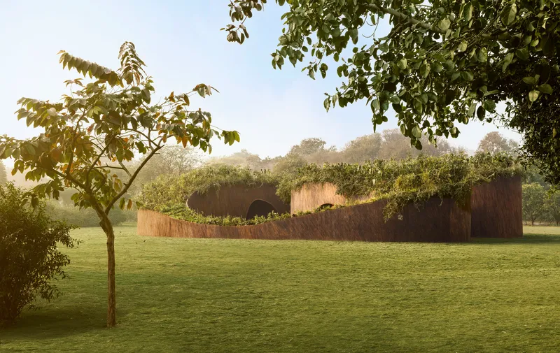 Curving rammed earth wall with planted green roof set in a mowed lawn under morning light