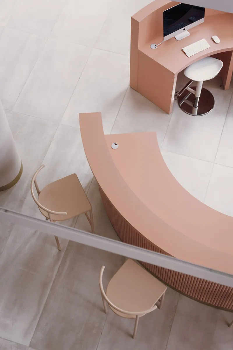 Overhead view of a curved pink reception desk with fluted edge on pale stone floor tiles
