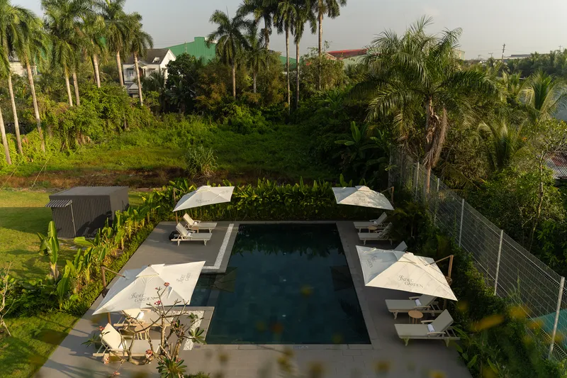Elevated view of rectangular pool deck with white umbrellas set within lush tropical garden landscape
