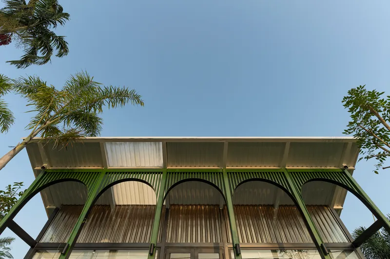 Upward view of the corrugated metal facade with green arched supports framed by palm fronds