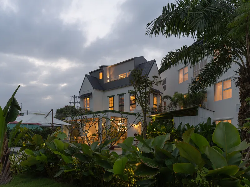 Rear view of the gabled roofline and illuminated windows rising above banana plants at dusk