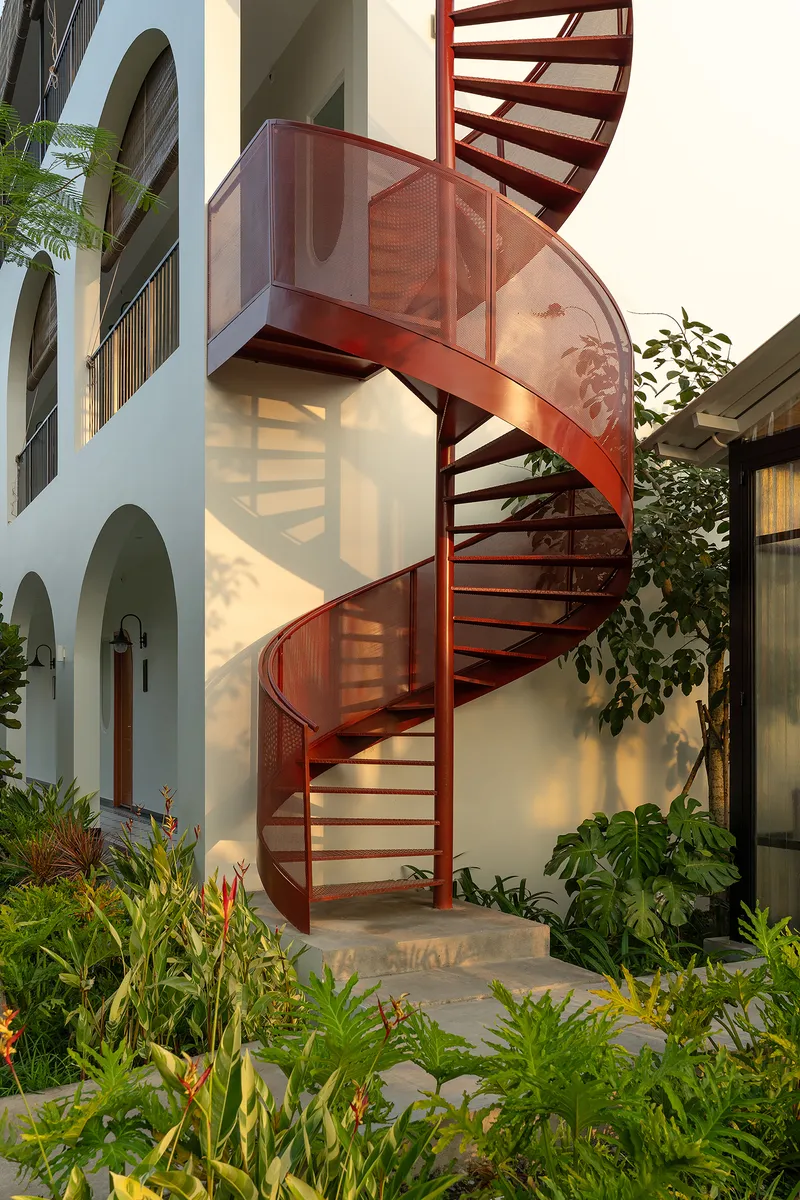 Close view of the red metal spiral staircase with perforated landing platform at golden hour