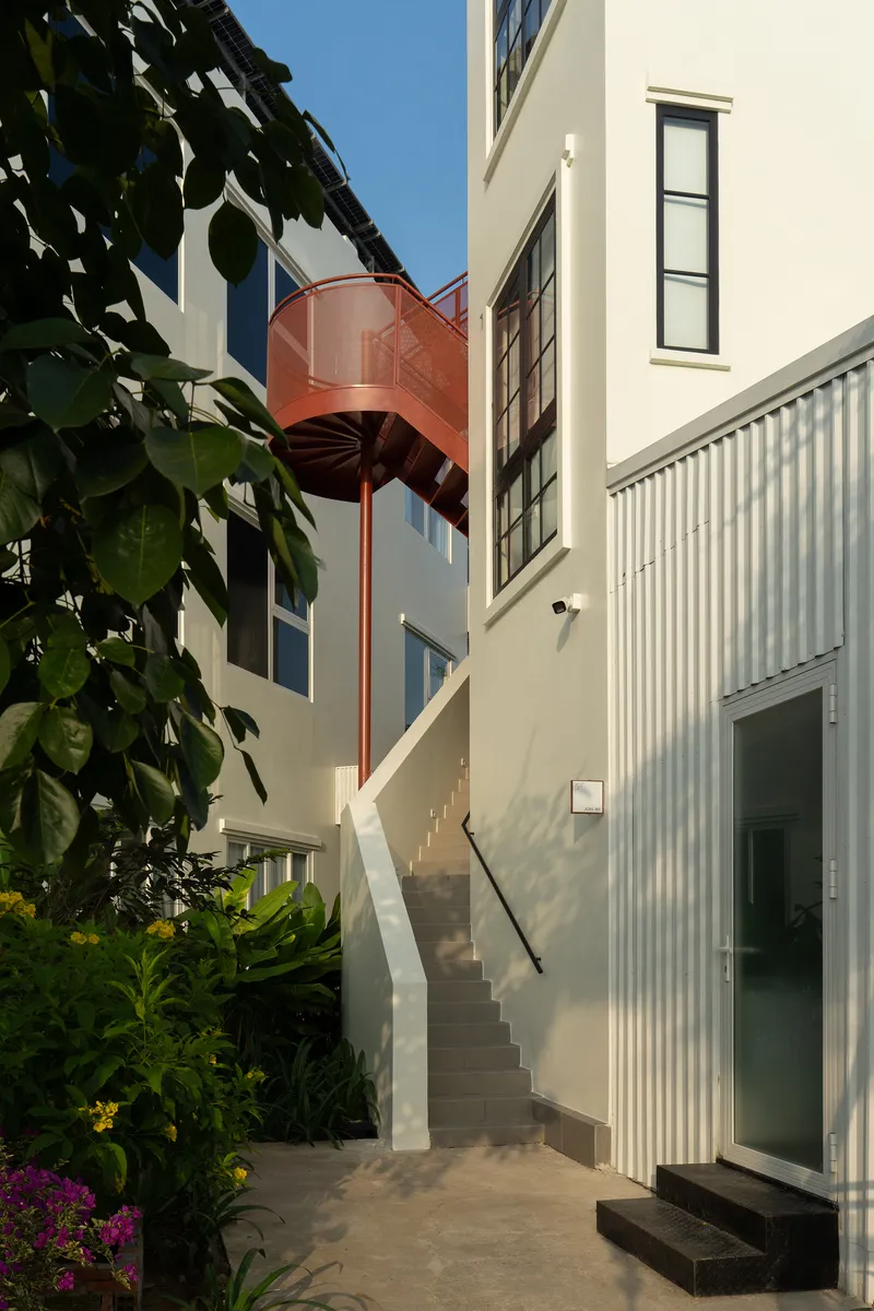 Exterior courtyard staircase with arched copper canopy connecting white rendered volumes and lush tropical planting