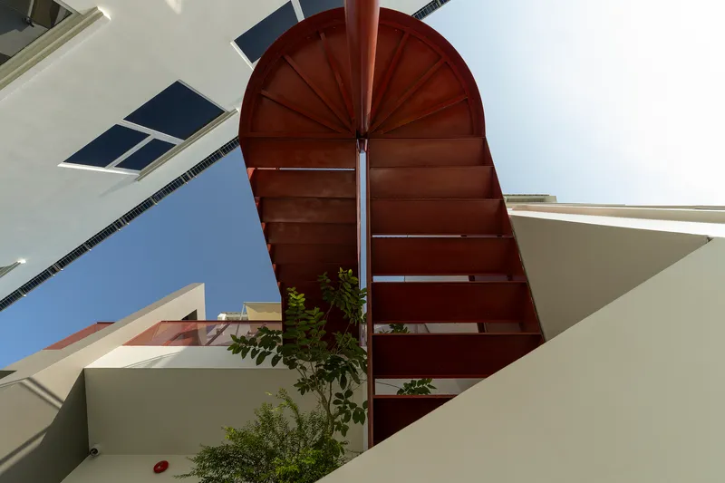 Upward view of arched copper staircase canopy with central steel pole and planted openings below