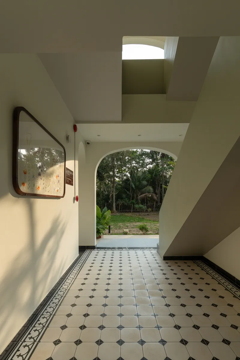 Entry hall with patterned tile floor and arched opening framing tropical vegetation beyond under skylight