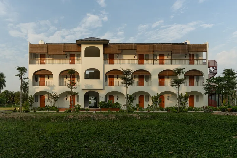 Three-storey facade with arched openings and timber-paneled balconies facing a grass lawn