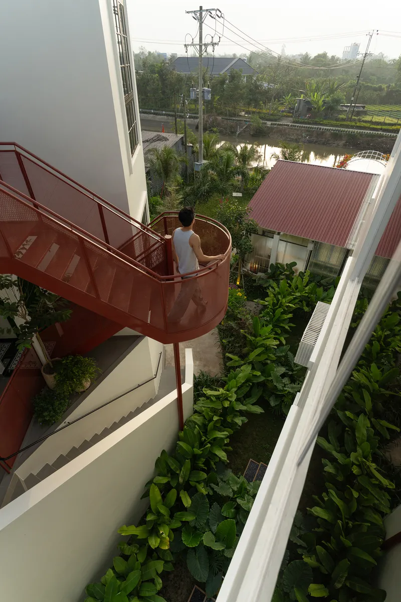 Overhead view of a person descending the spiral stair with corrugated roofs and pond visible beyond
