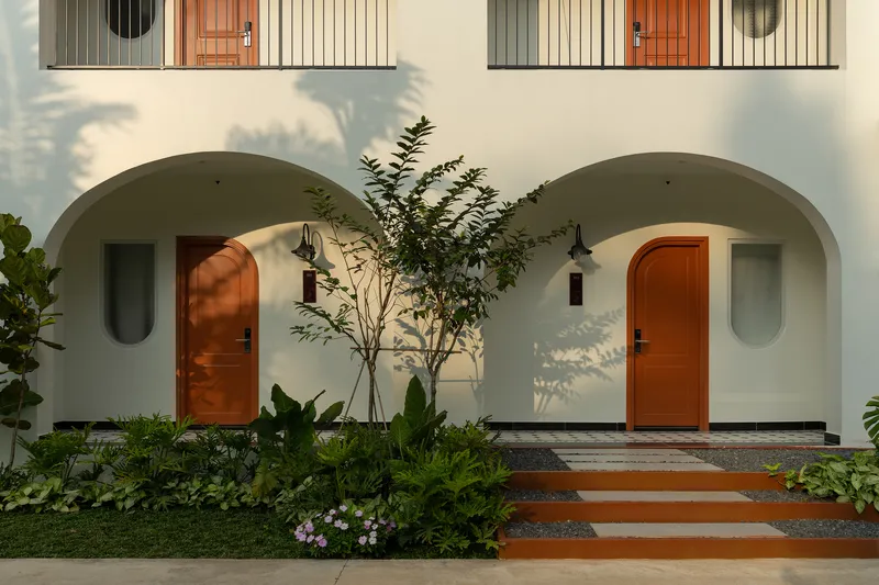 Paired arched entry alcoves with timber doors and oval windows casting afternoon shadows