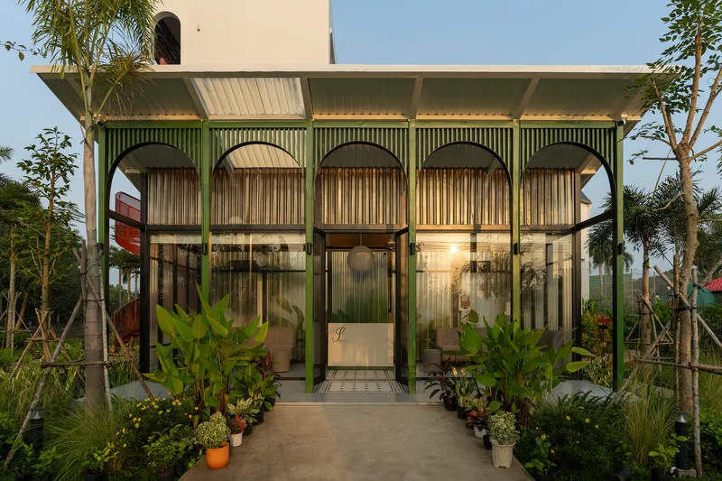Entry facade with arched corrugated metal screens and planted tropical landscape at dusk