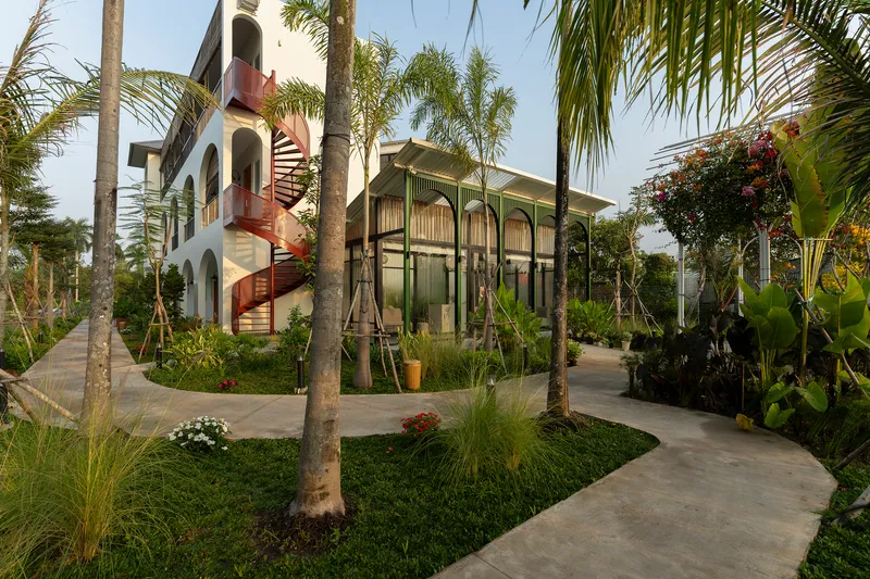 Garden pathways winding through palm trees toward the screened pavilion and residential block