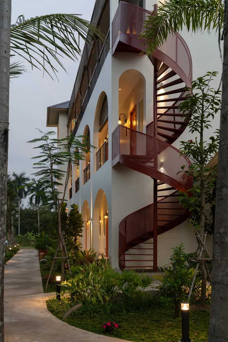 Exterior red steel spiral staircase ascending three stories along the white stucco facade at twilight