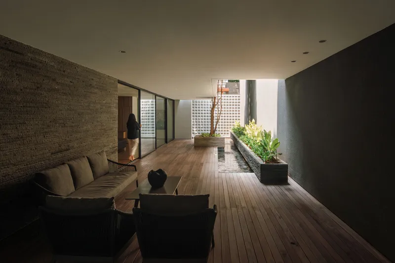 Timber-decked corridor with planters and a brick wall opening to a courtyard with natural light