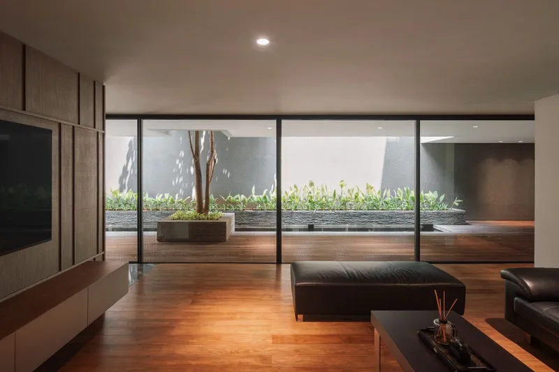 Living room with floor-to-ceiling glass wall overlooking a courtyard with a single tree at dusk