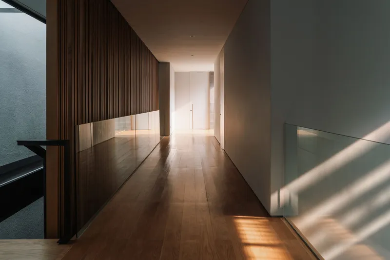 Corridor with ribbed timber wall and low glass balustrade illuminated by sunlight
