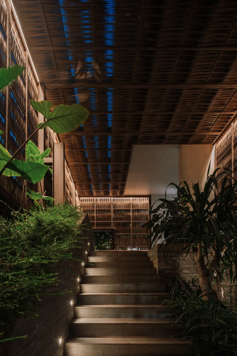 Staircase with timber treads ascending through a planted courtyard under a slatted wood ceiling