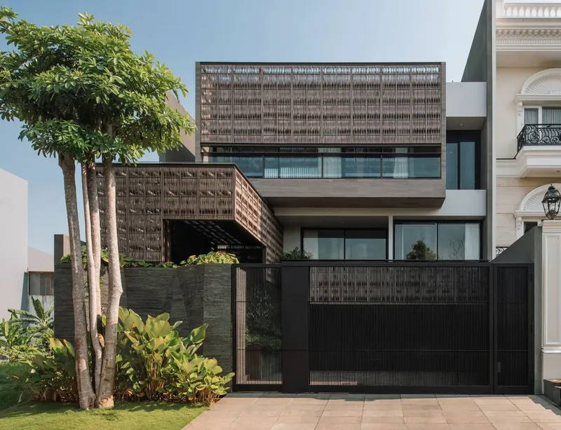 Street facade with stacked volumes clad in woven lattice screens and black metal gate framed by tropical trees