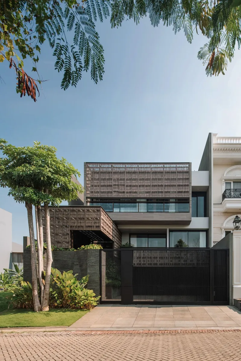 Front elevation showing layered lattice screens and cantilevered upper volume seen through leafy tree branches