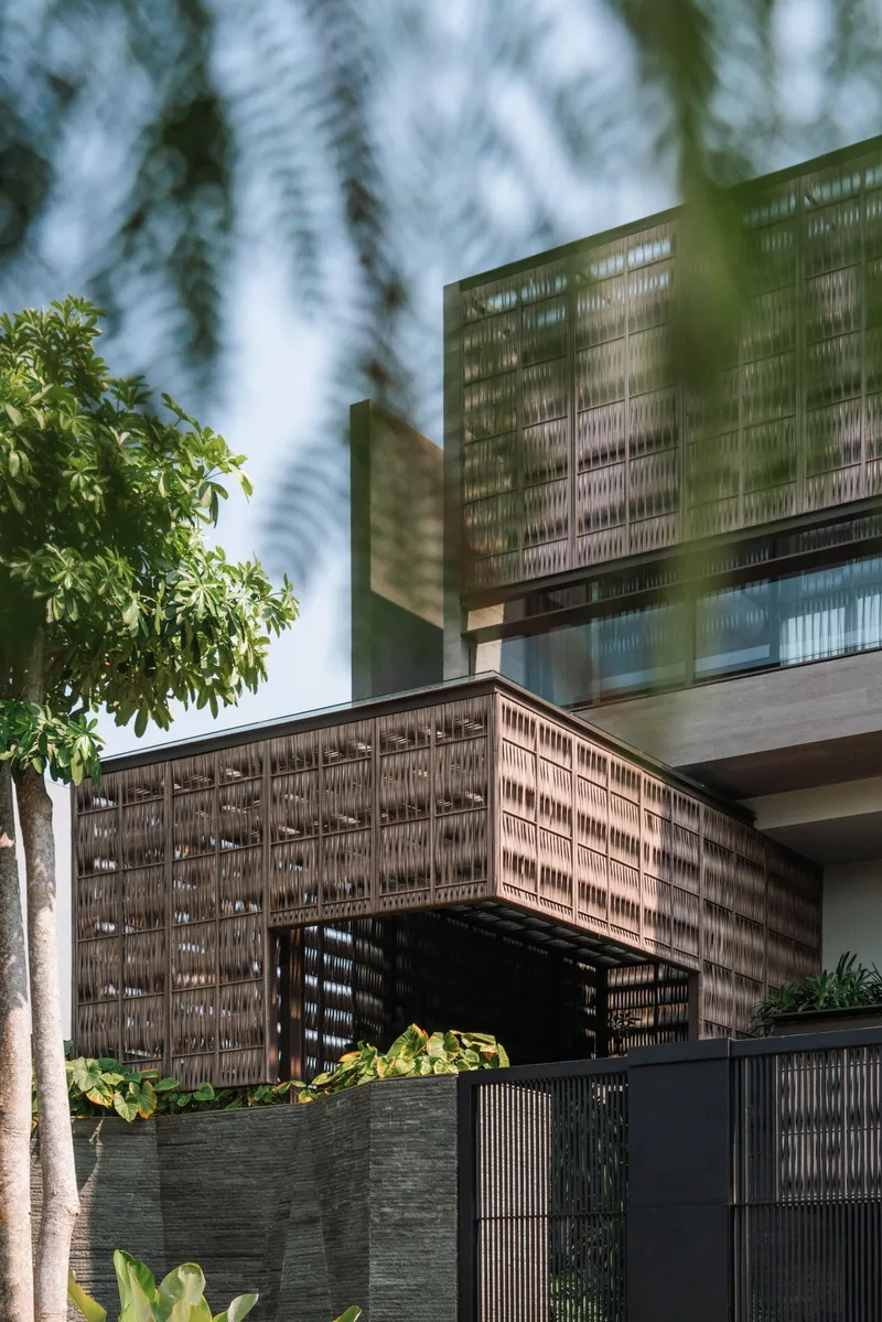 Upward view of the cantilevered facade with woven screening panels filtering dappled sunlight through foliage