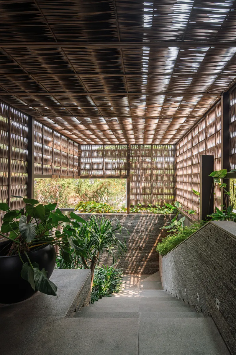 Interior terrace enclosed by woven lattice walls and ceiling creating filtered light patterns over planted beds