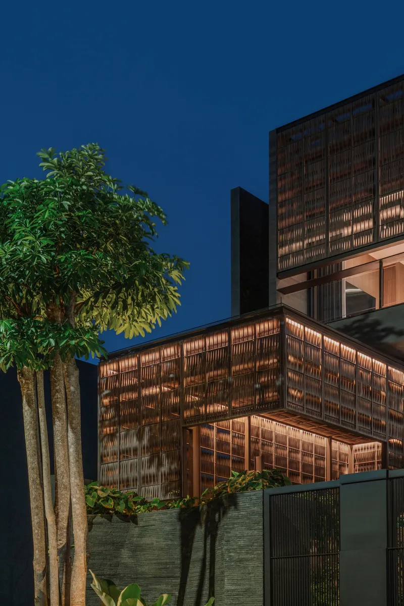 Exterior view of the layered timber screen facade and planted tree at twilight