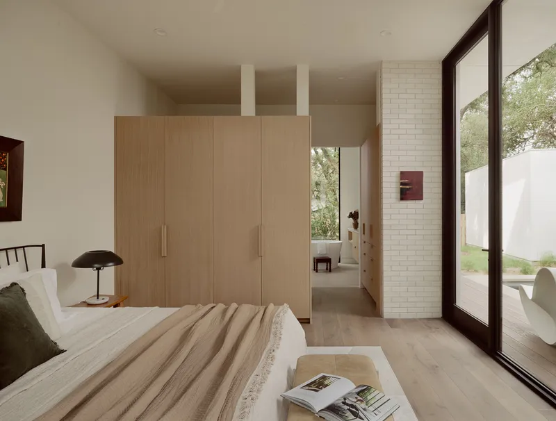 Bedroom with floor-to-ceiling dark-framed glazing opening to a courtyard framed by mature trees