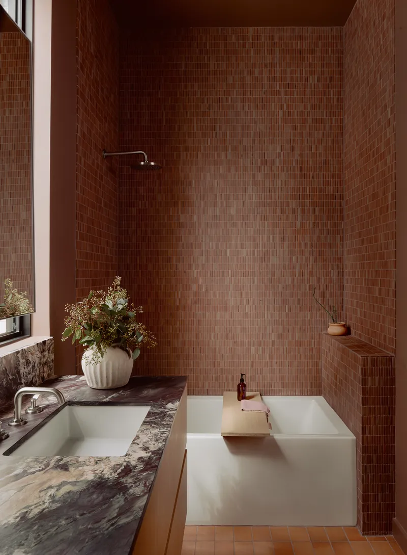 Bath alcove clad entirely in small brown mosaic tiles with freestanding tub and overhead shower