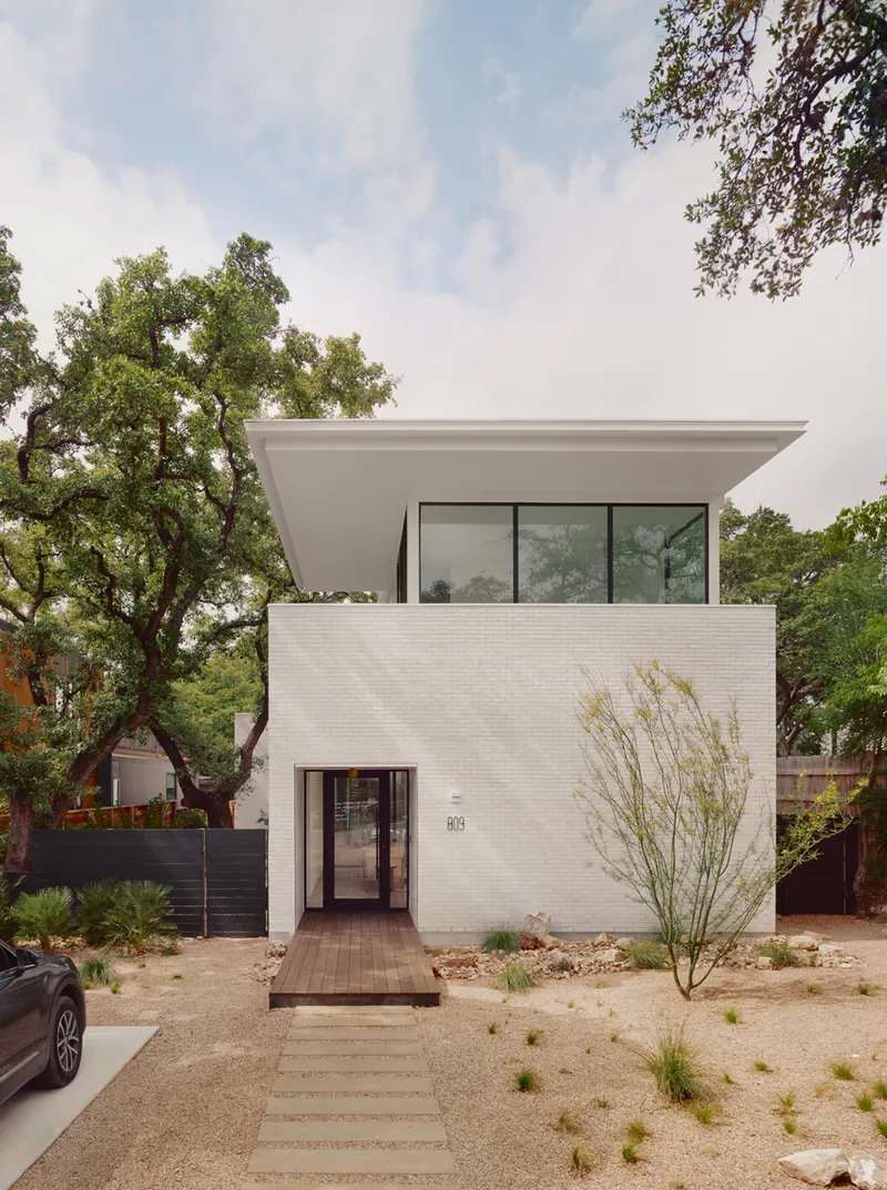 Street view of white brick facade with cantilevered upper volume and native desert plantings