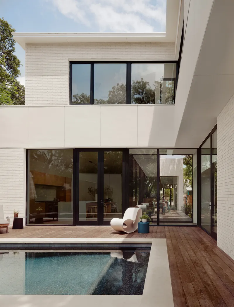 Rear courtyard with timber deck, rectangular pool, and floor-to-ceiling glazing on two levels