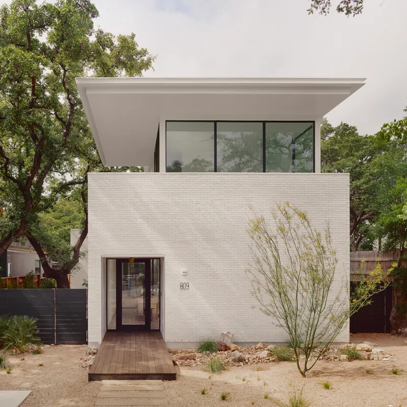 Street facade with white brick and recessed glazed entry flanked by a desert landscape with grasses