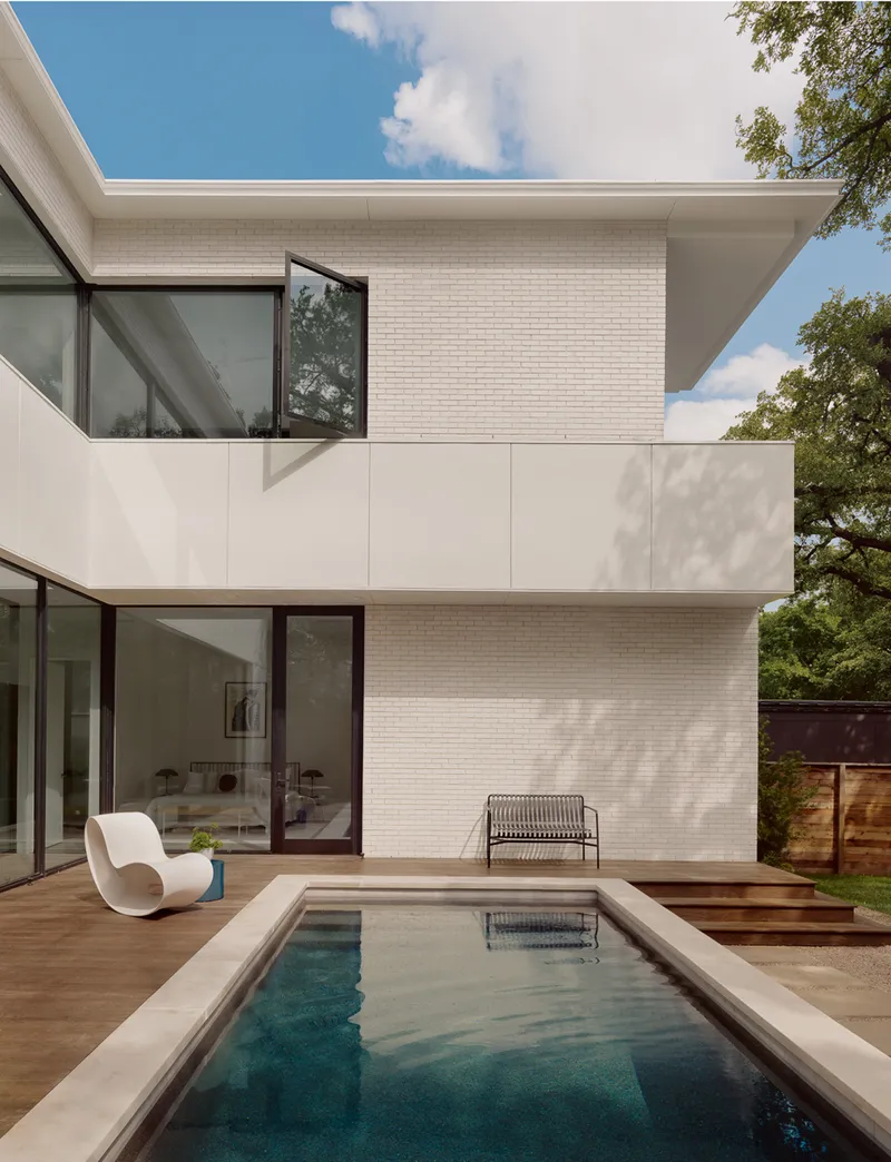 Rear elevation showing white brick volumes and a pool deck under scattered clouds