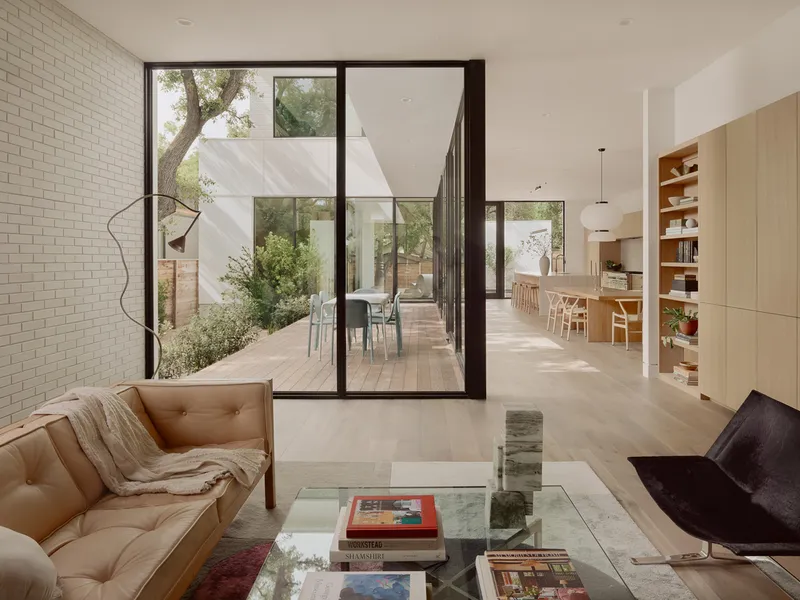 Living area opening to a courtyard through floor-to-ceiling glazed doors with white brick wall